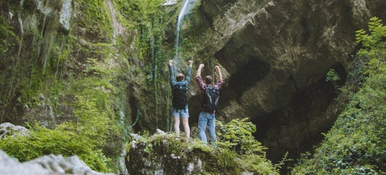 dvoje ljudi stoji na steni i gleda vodopad
