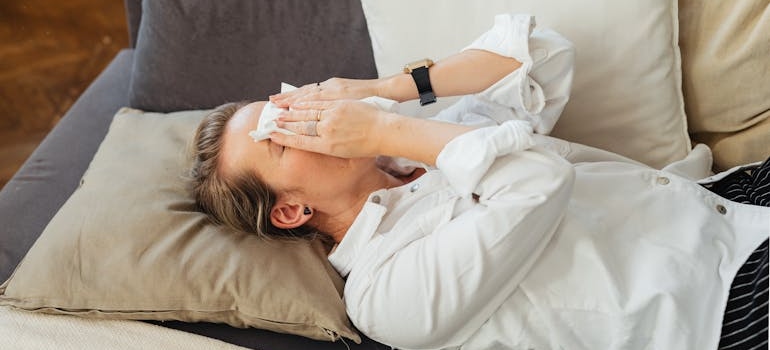 žena leži na krevetu sa maramicom na nosu