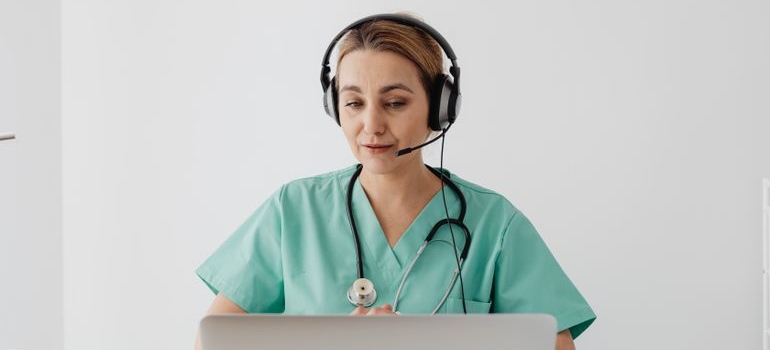 Lekar sa slušalicama ispred laptopa pruža online savetovanje pacijentu