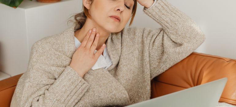 žena sa simptomima gripa sedi na kauču i drži se za grlo